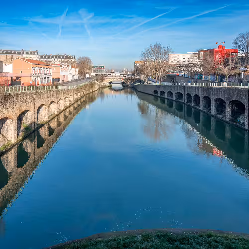 Canal Saint-Denis waterfront in Saint-Denis, Île-de-France near Paris, with arched stone embankments and city skyline, a top sightseeing spot for scenic walks and local attractions.