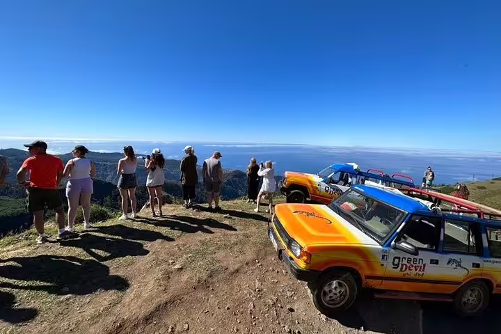 Tourists enjoy scenic ocean views from a cliffside in rugged 4x4 Jeeps during a full-day adventure to Porto Moniz and Fanal.