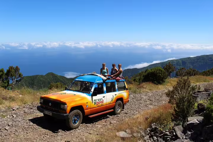 Tourists enjoy scenic views from a colorful 4x4 Jeep in Porto Moniz and Fanal, Madeira, under a clear blue sky.