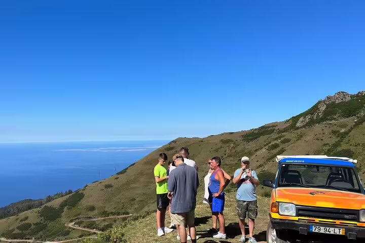 Tourists enjoy breathtaking views in Madeira's mountains during a 4x4 Jeep tour to Porto Moniz and Fanal under a clear blue sky.