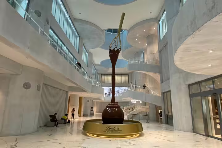Inside the Lindt Factory, showcasing a grand chocolate sculpture centerpiece in a modern, spacious atrium.
