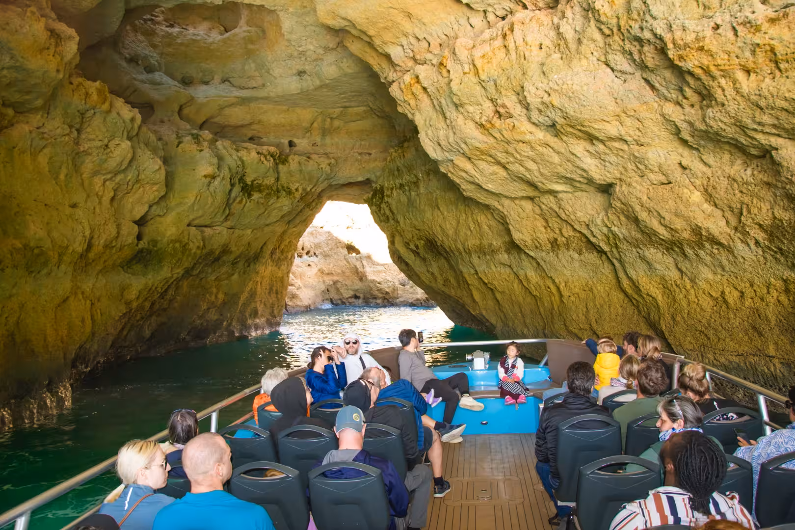 Tourists on a boat exploring the stunning Benagil Caves with turquoise waters and limestone formations in Algarve.