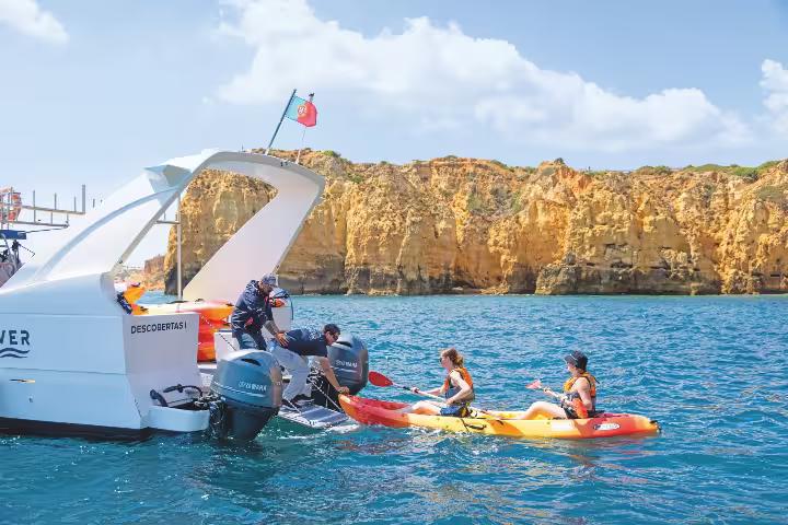 Kayakers launching from a boat near golden cliffs in Lagos Algarve Portugal on a sunny kayak tour adventure