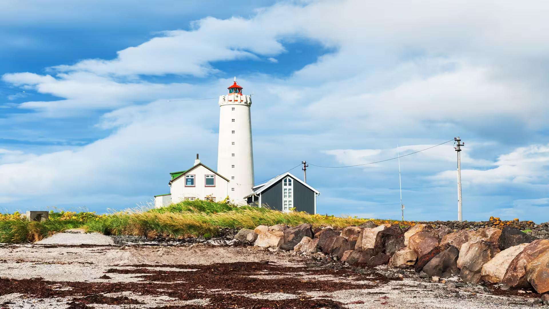 Scenic Icelandic lighthouse with rocky shoreline and lush greenery on a Reykjavik elves and nature driving tour