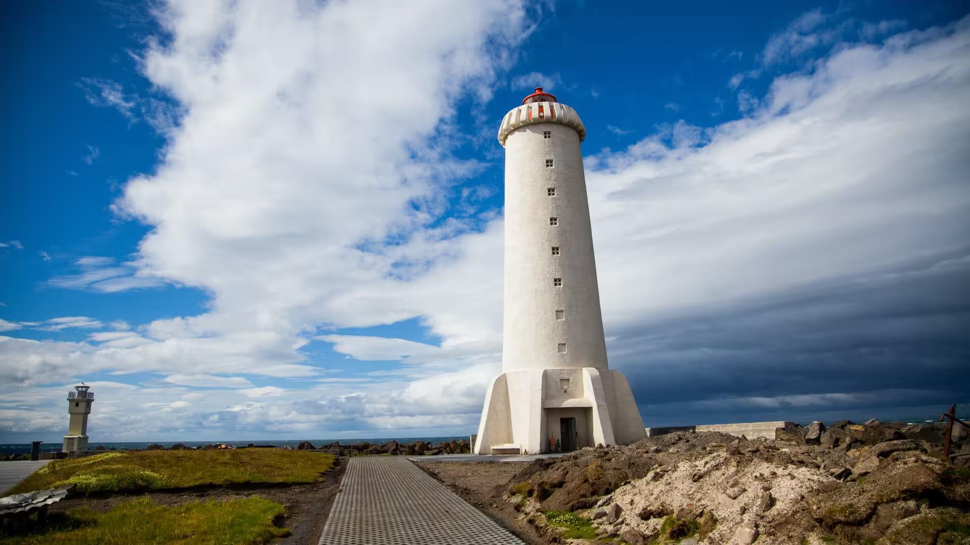 Iconic white Reykjavik lighthouse on rocky coastline under dramatic blue sky on Iceland elves nature driving tour