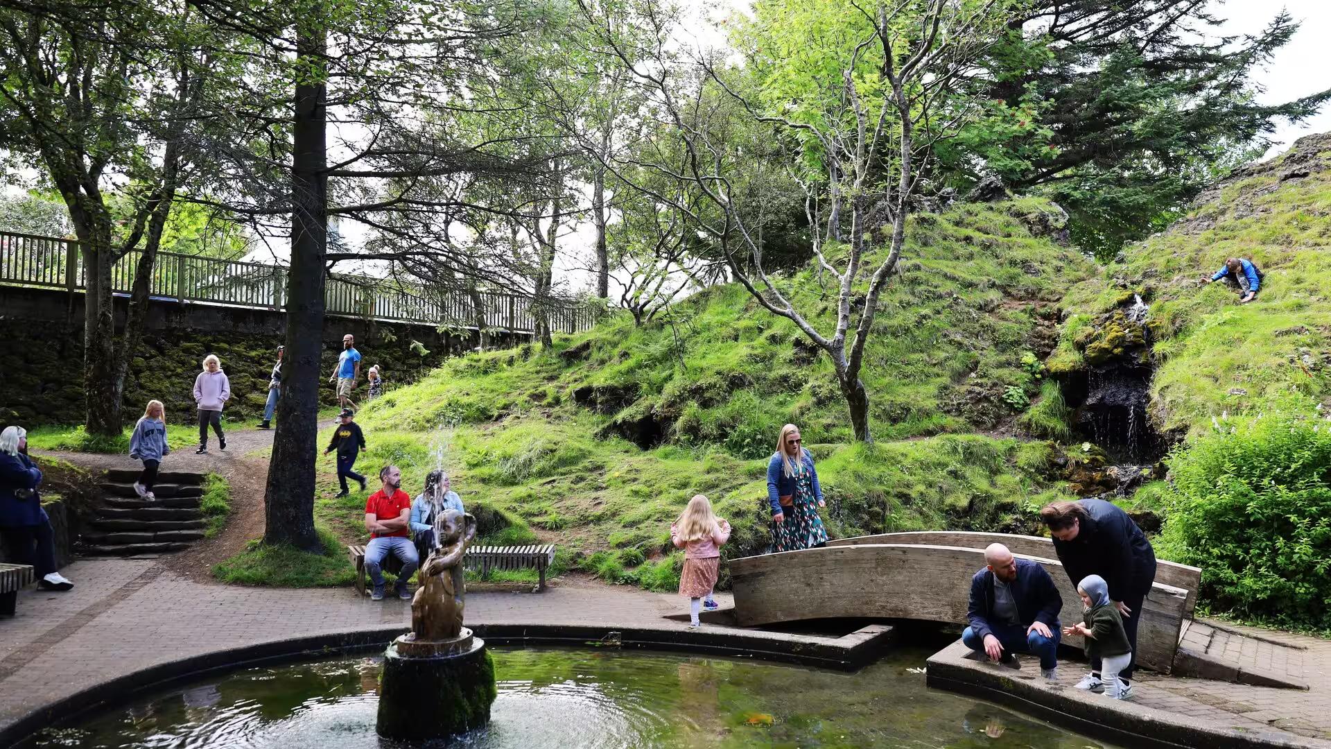Visitors exploring lush green Reykjavik park with fountain and waterfall on guided Iceland elves nature driving tour