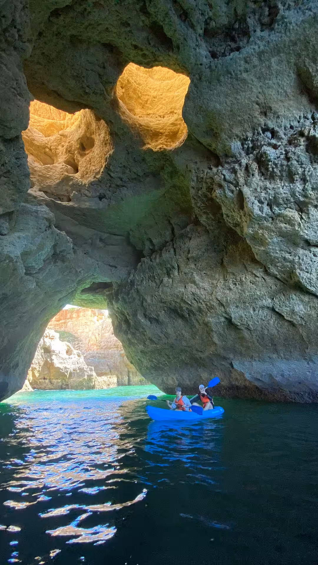 Kayakers paddle through the shadowy Benagil sea cave in Algarve, Portugal, past glowing rock arches and emerald water.