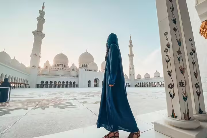 Visitor exploring the Sheikh Zayed Grand Mosque's stunning courtyard during the Abu Dhabi City Tour from Dubai.
