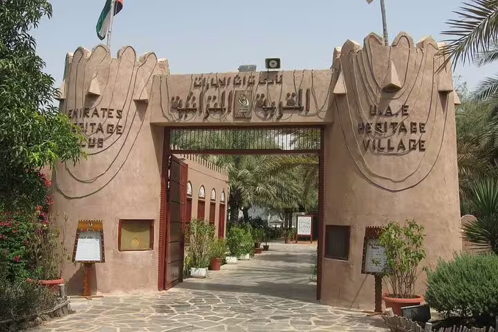 Entrance to UAE Heritage Village in Abu Dhabi surrounded by lush greenery, showcasing cultural experiences on city tours.