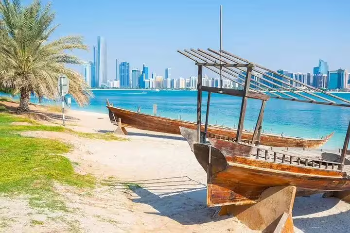 Traditional wooden boats on Abu Dhabi beach with city skyline in the background, highlighting cultural and modern contrasts.