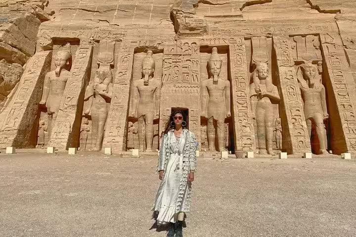 Visitor posing before Abu Simbel Temple statues on a day tour from Aswan, ancient Egyptian reliefs and columns