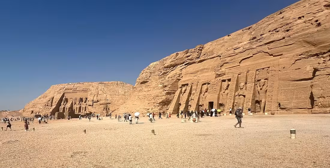 Tourists explore the ancient rock-cut temples of Abu Simbel under a clear blue sky, highlighting Egypt's historical grandeur.