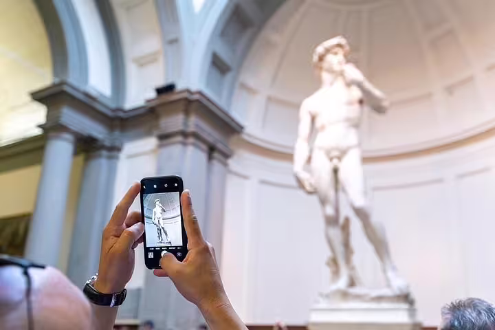 Visitor photographing Michelangelo’s David inside Florence’s Accademia Gallery during a live guided skip-the-line tour