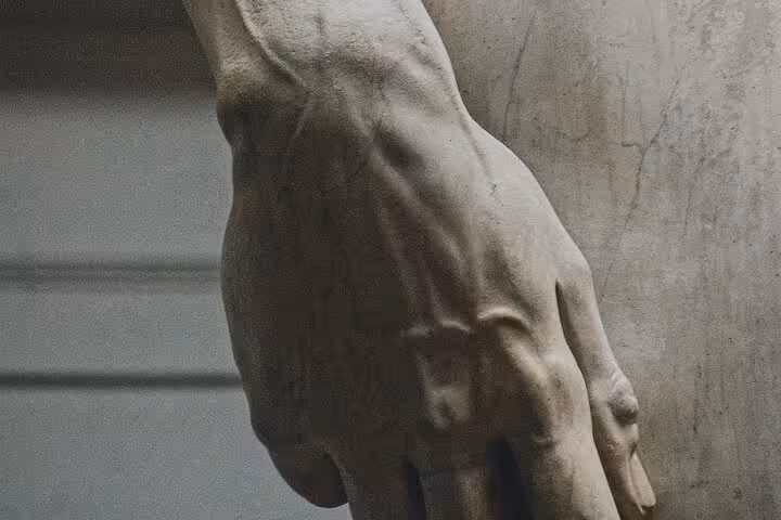 Detailed view of a statue's hand showcasing intricate craftsmanship at Accademia Gallery, Florence.