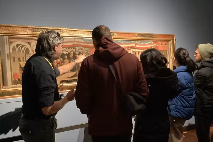 Tour guide explains a detailed historic painting to a small group at the Accademia Gallery in Florence.
