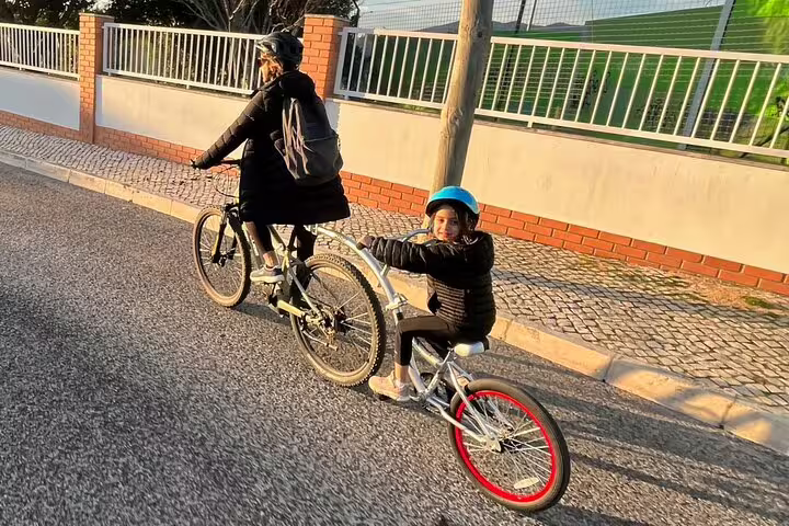 Adult and child tandem biking on sunny Cascais road during relaxed e-bike tour.