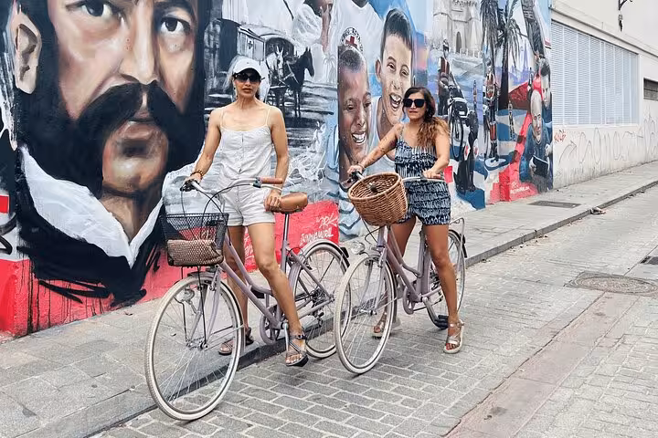 Two women with city rental bikes pose by colorful street mural, ideal adult city bike rental sightseeing