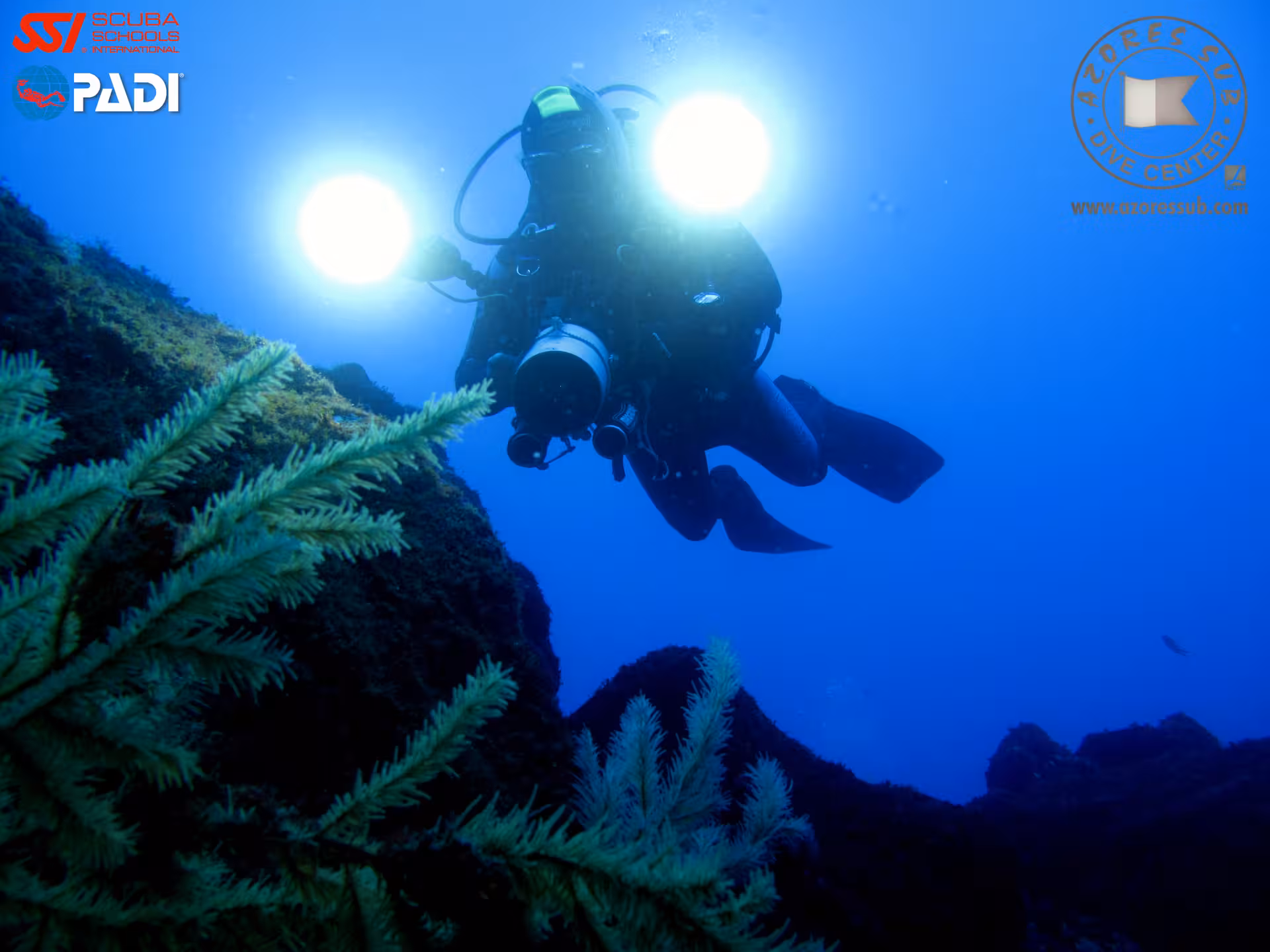 Advanced Open Water Diver night dive training, scuba diver with twin lights hovering above reef in deep blue ocean