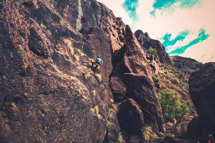 Adventurer scaling a rugged rock face in a lush rainforest canyon, perfect for thrilling canyoning experiences.