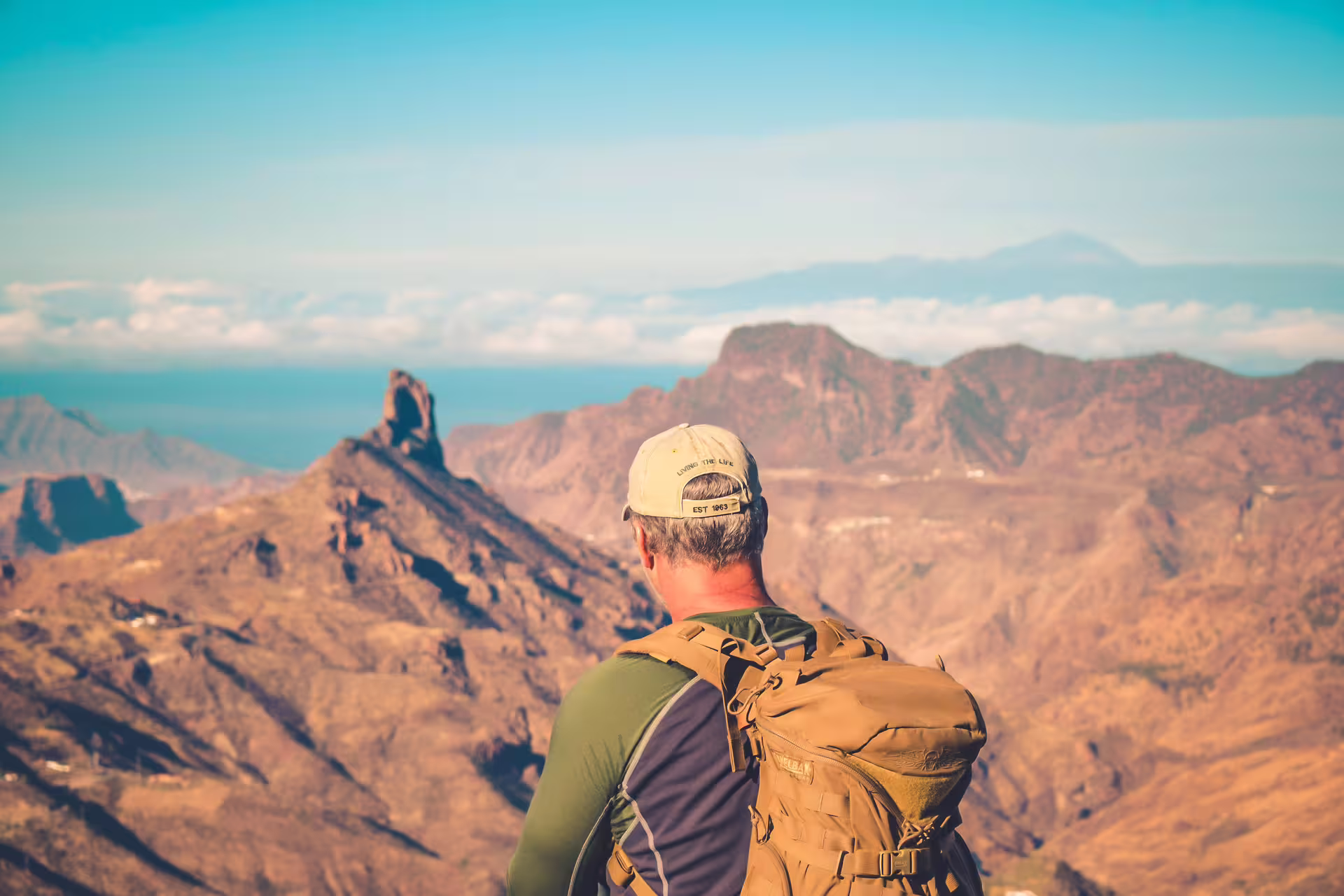 Adventurer with backpack gazing at stunning volcanic landscape on Volcano Heart Tour, under clear blue skies.