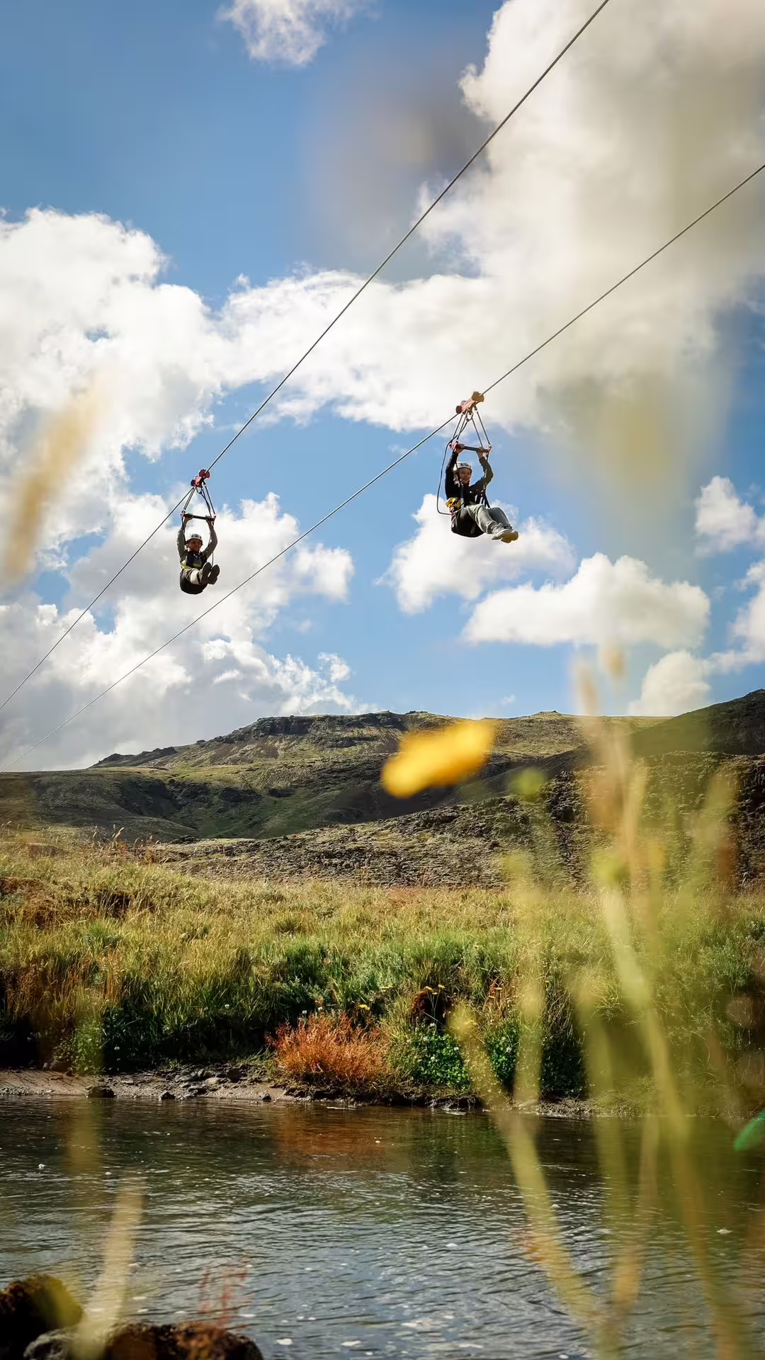 Two adventurers zip-lining over scenic landscapes under a bright blue sky, showcasing an exhilarating outdoor experience.