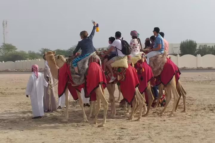 Group enjoying camel ride on sandy terrain, led by guides, during an afternoon desert safari tour.