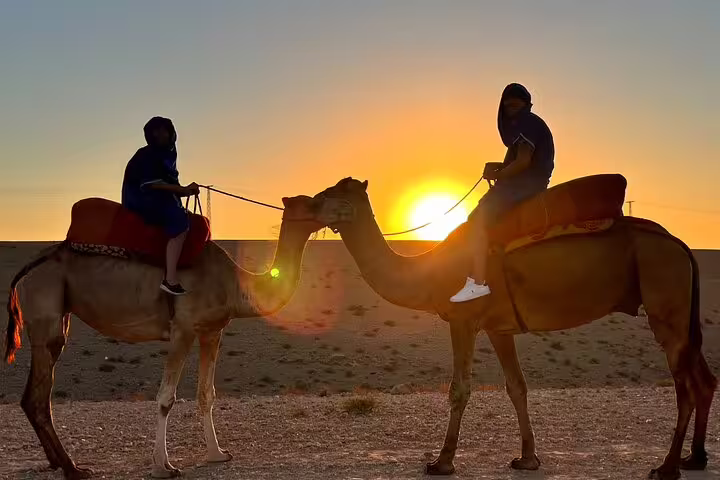 Two riders on camels at golden sunset in Agafay Desert, Marrakech camel ride tour with scenic dunes