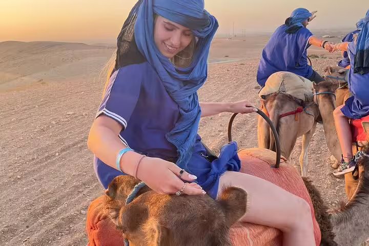 Traveler in blue scarf petting camel during Agafay Desert sunset camel ride tour from Marrakech, Morocco