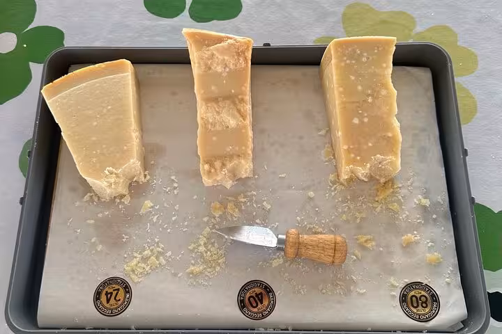 Three aged Parmesan cheese wedges with a cheese knife on display, featured in an Italian culinary tour.