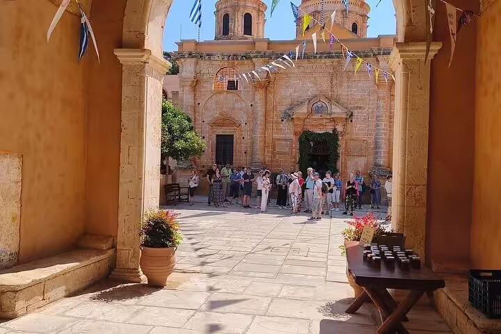 Visitors explore the historic Agia Triada Monastery courtyard in Chania, surrounded by vibrant flowers and ancient architecture.