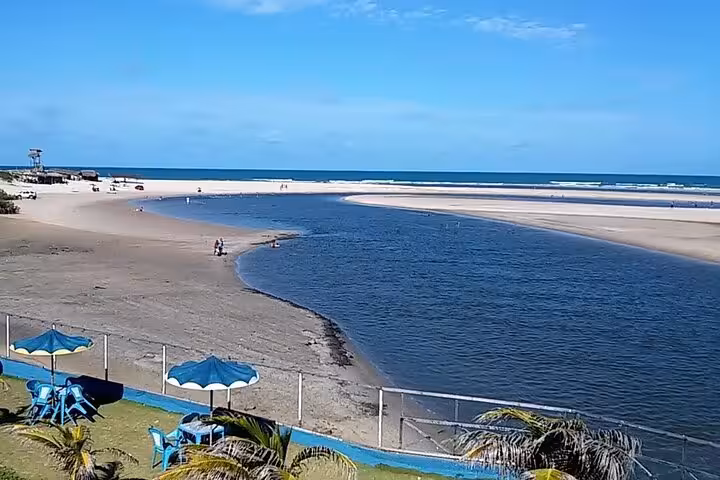 River meeting the sea at Águas Belas, Ceará, with lagoon views and beach umbrellas on a coastal tour