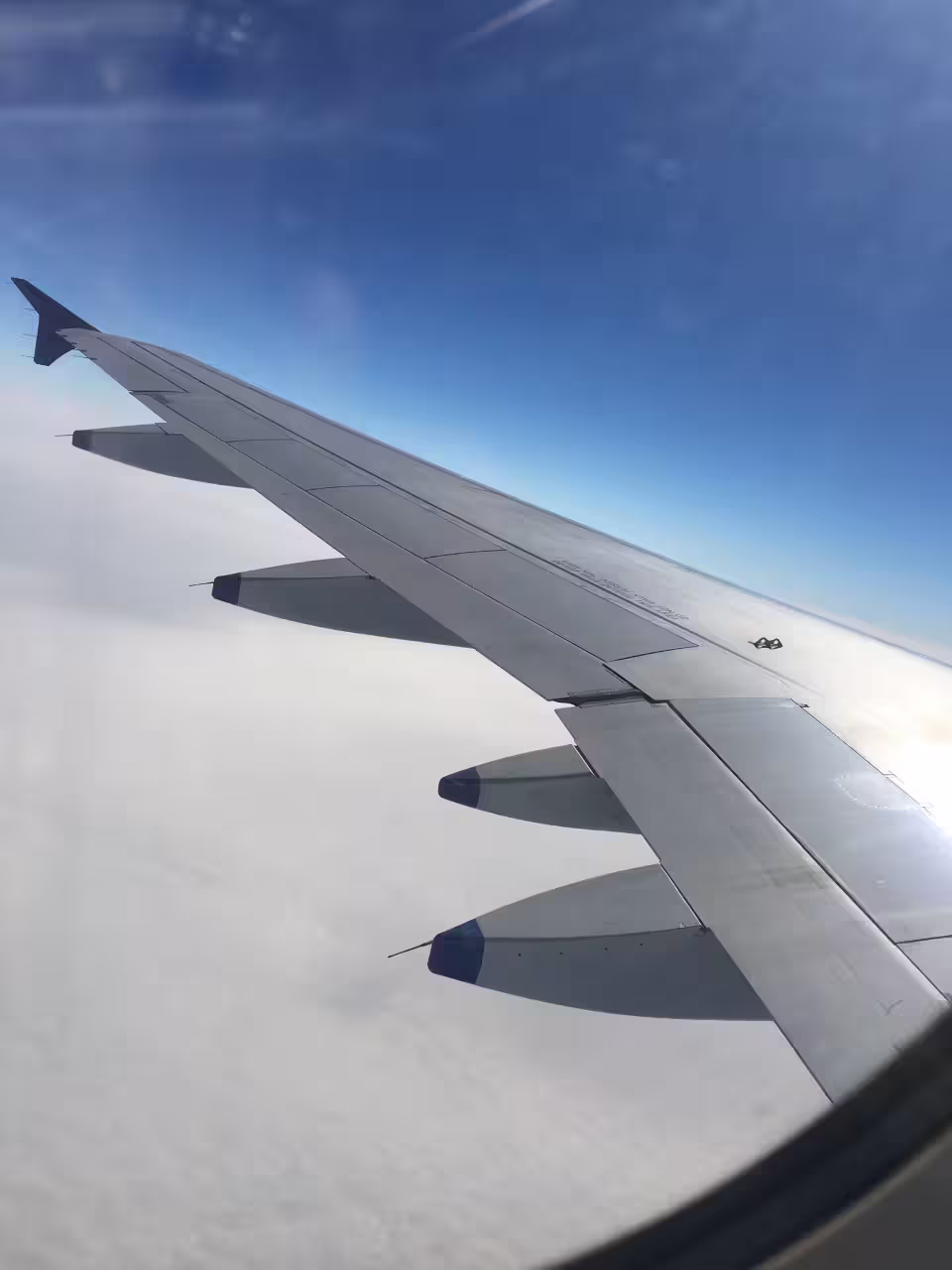 View from airplane window showcasing wing above fluffy clouds and clear blue sky, ideal for travel enthusiasts and adventure seekers.