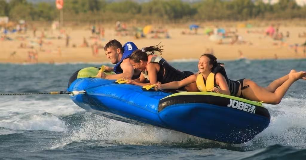 Friends enjoy a thrilling Airstream inflatable tube ride over turquoise waves near a lively summer beach resort