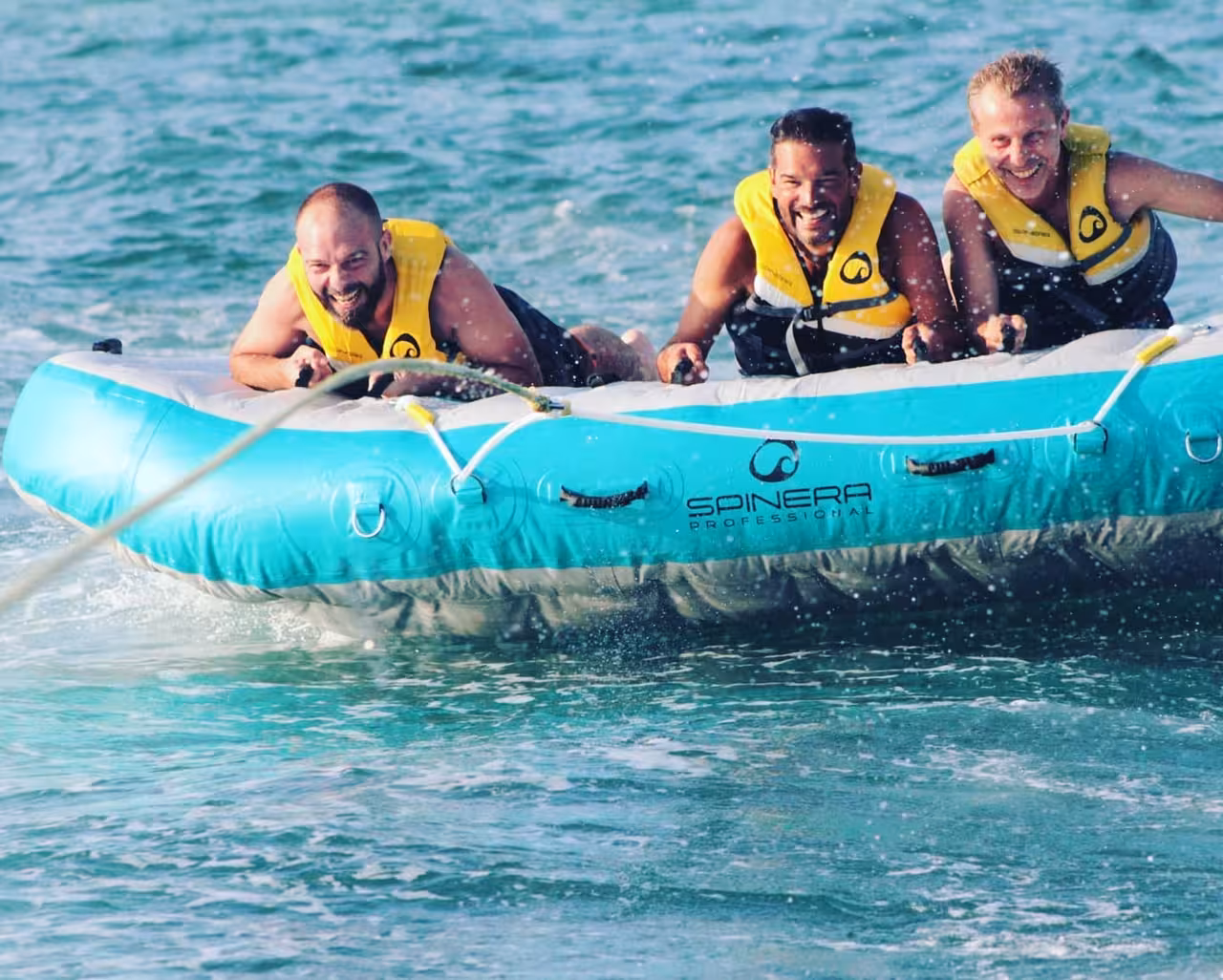 Laughing adults holding tight on Airstream towable raft, skimming fast over clear water during Algarve boat tour