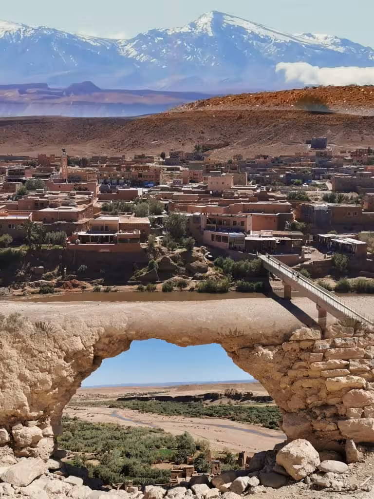 Ait Benhaddou and Ounila Valley framed by a stone arch with snowy Atlas Mountains on a Best of Morocco trip