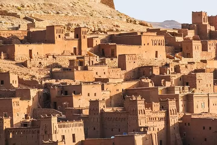 Ait Benhaddou's ancient kasbahs bask in golden sunlight, a highlight on the Morocco desert tour from Fes to Marrakech.