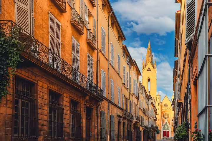 Charming street in Aix-en-Provence with colorful buildings leading to a historic church under a bright blue sky.