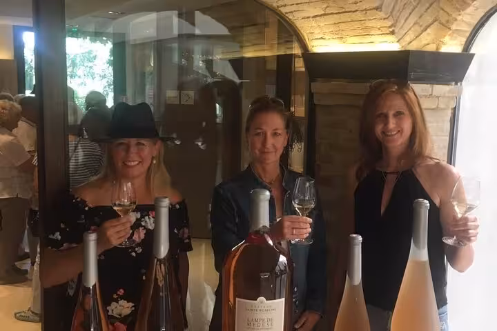 Three women enjoying a wine tasting session inside a cozy winery in Aix En Provence, with bottles displayed in the foreground.