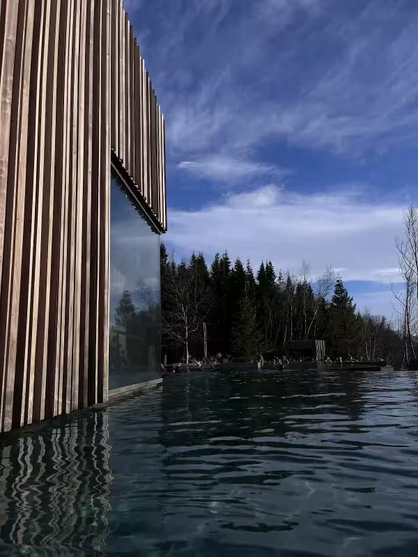 Infinity pool beside modern wooden clad building with evergreen forest and blue sky in Akureyri Iceland