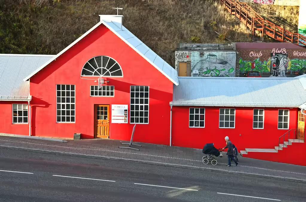 Bright red building in Akureyri Iceland with person pushing stroller along street
