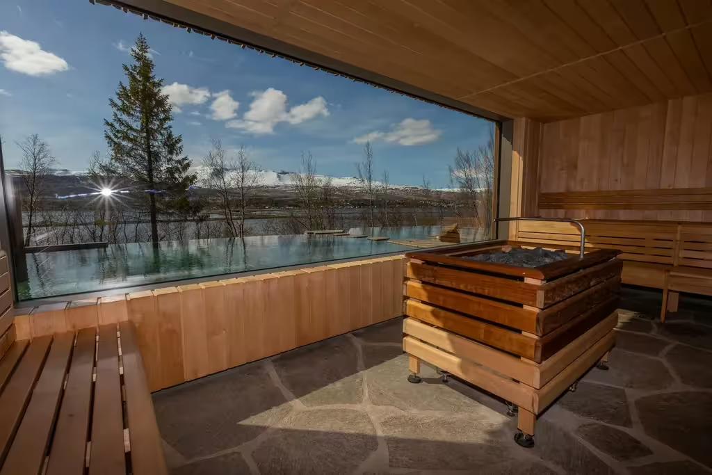 Wooden sauna interior with panoramic window overlooking snowy mountains and lake in Akureyri, Iceland