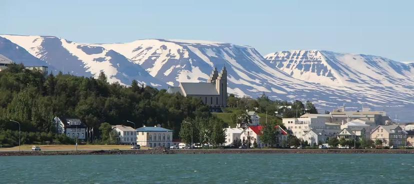 Akureyri town waterfront with snow-capped mountains and Akureyrarkirkja church on hilltop, Iceland
