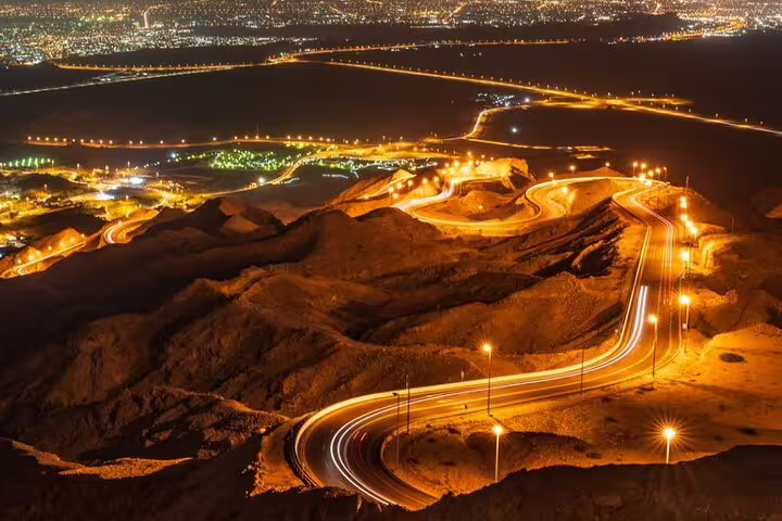 Scenic night view of Al Ain's illuminated winding roads from Jebel Hafeet on a private garden city tour.
