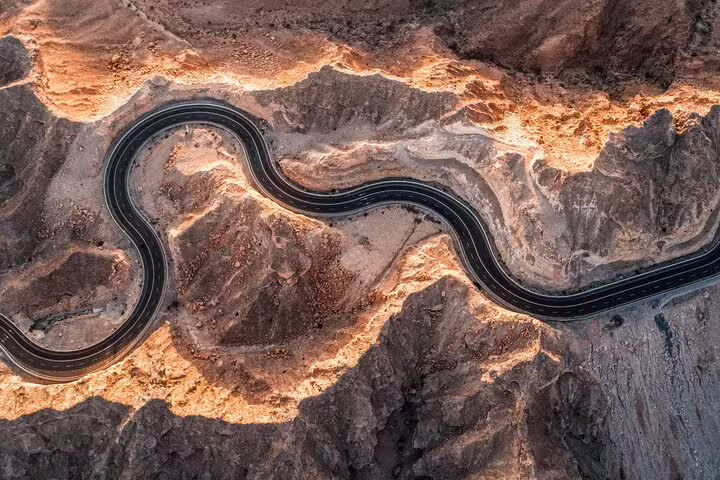 Aerial view of a winding mountain road in Al Ain, showcasing scenic desert landscapes on a garden city tour.