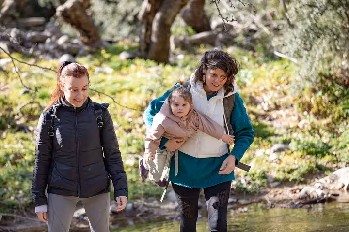 Two women hiking with a young child by a clear stream on the family-friendly Alama Spring trail in Ikaria