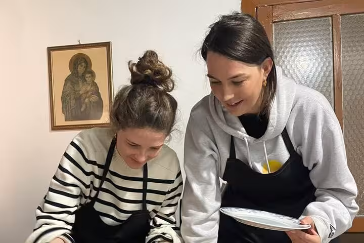 Two women in aprons enjoy a hands-on cooking class in Albania, preparing dishes during a private guided tour.