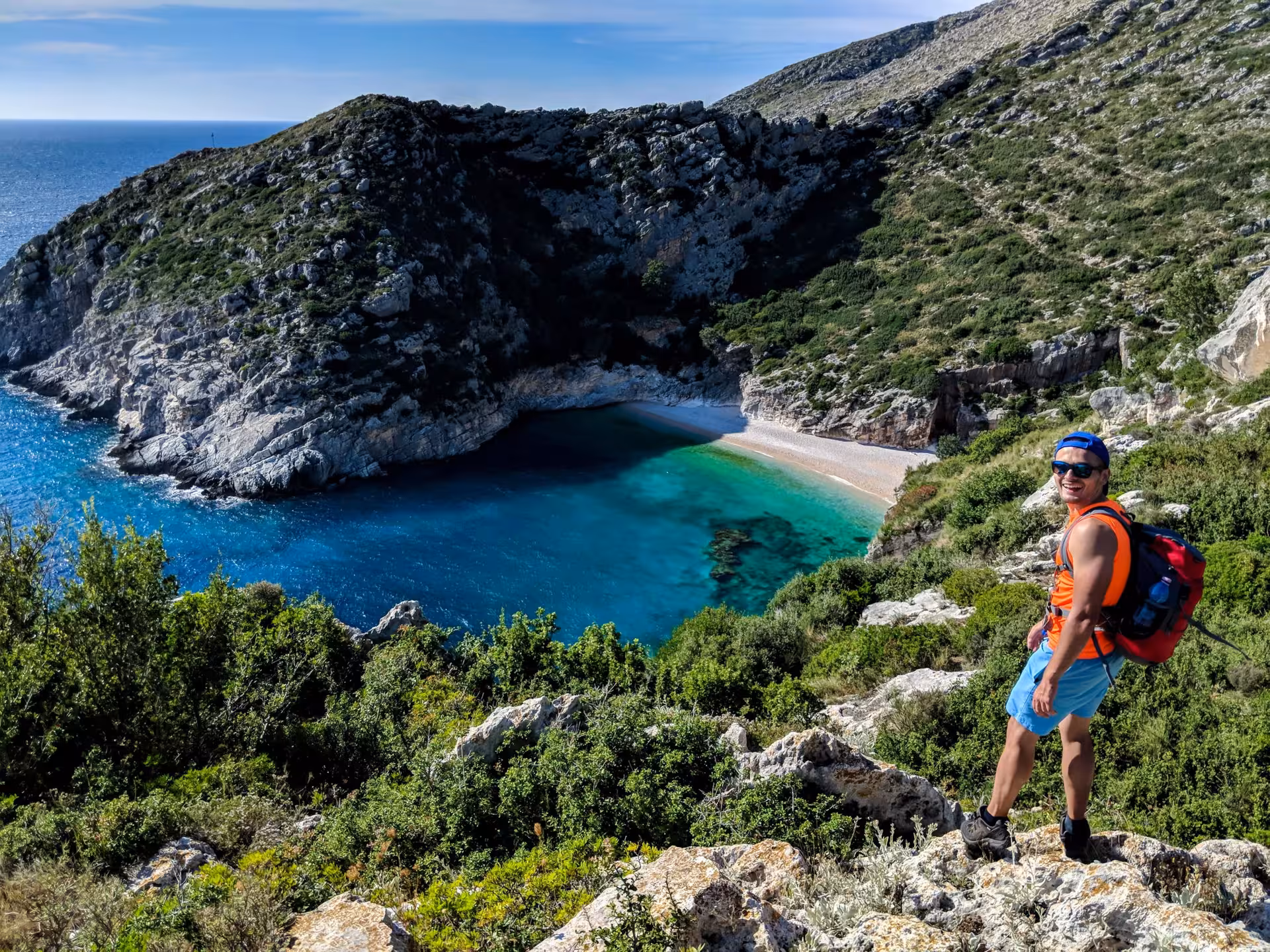 Traveler with backpack overlooking a secluded, turquoise bay and rugged cliffs, perfect for adventure and exploration.