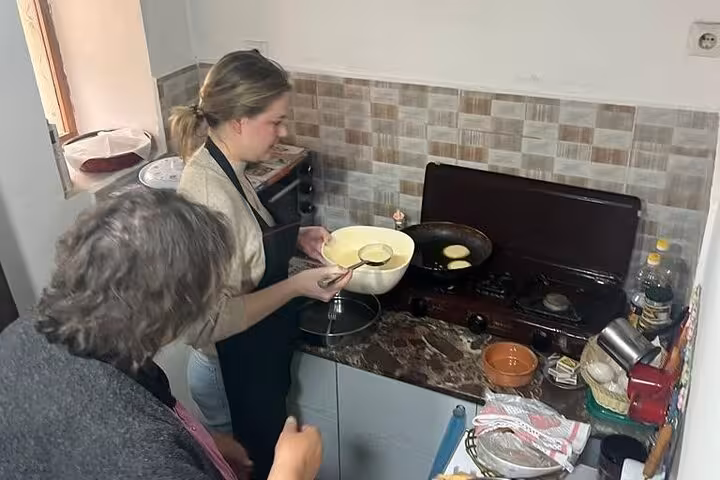 Two participants prepare traditional Albanian pancakes in a cozy kitchen as part of a private guided tour.
