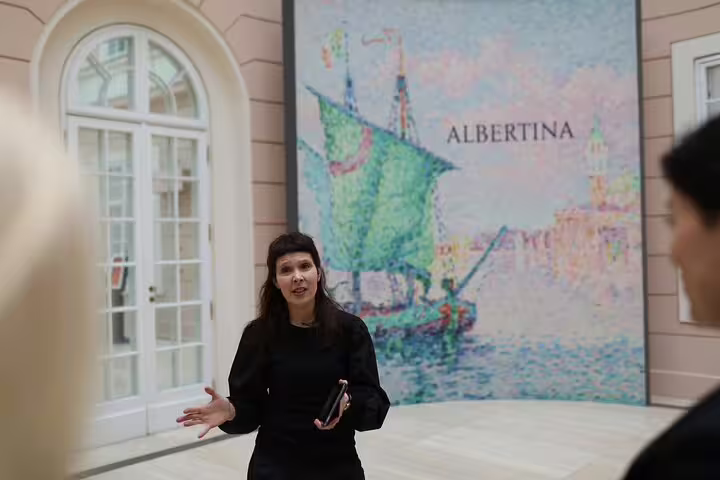 Art guide explains masterpiece in the Albertina Museum with vibrant art backdrop on private tour.