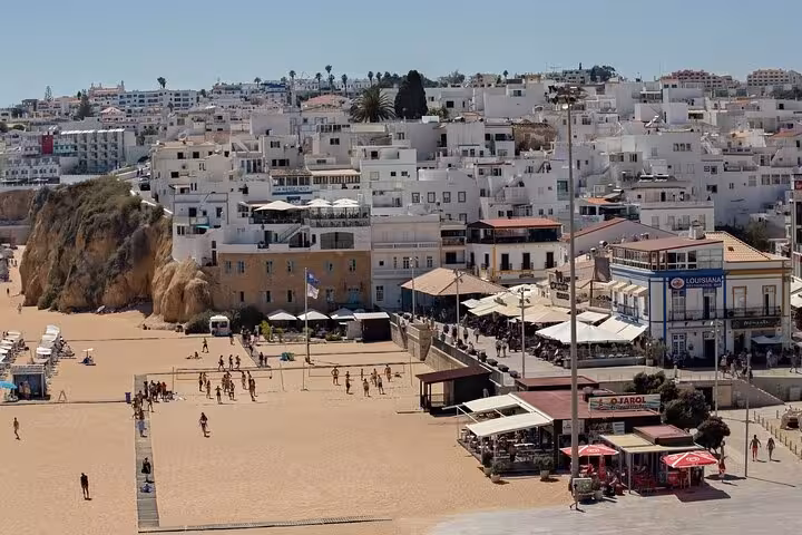 Vibrant Albufeira beach scene with people enjoying the sun and surrounding whitewashed buildings.